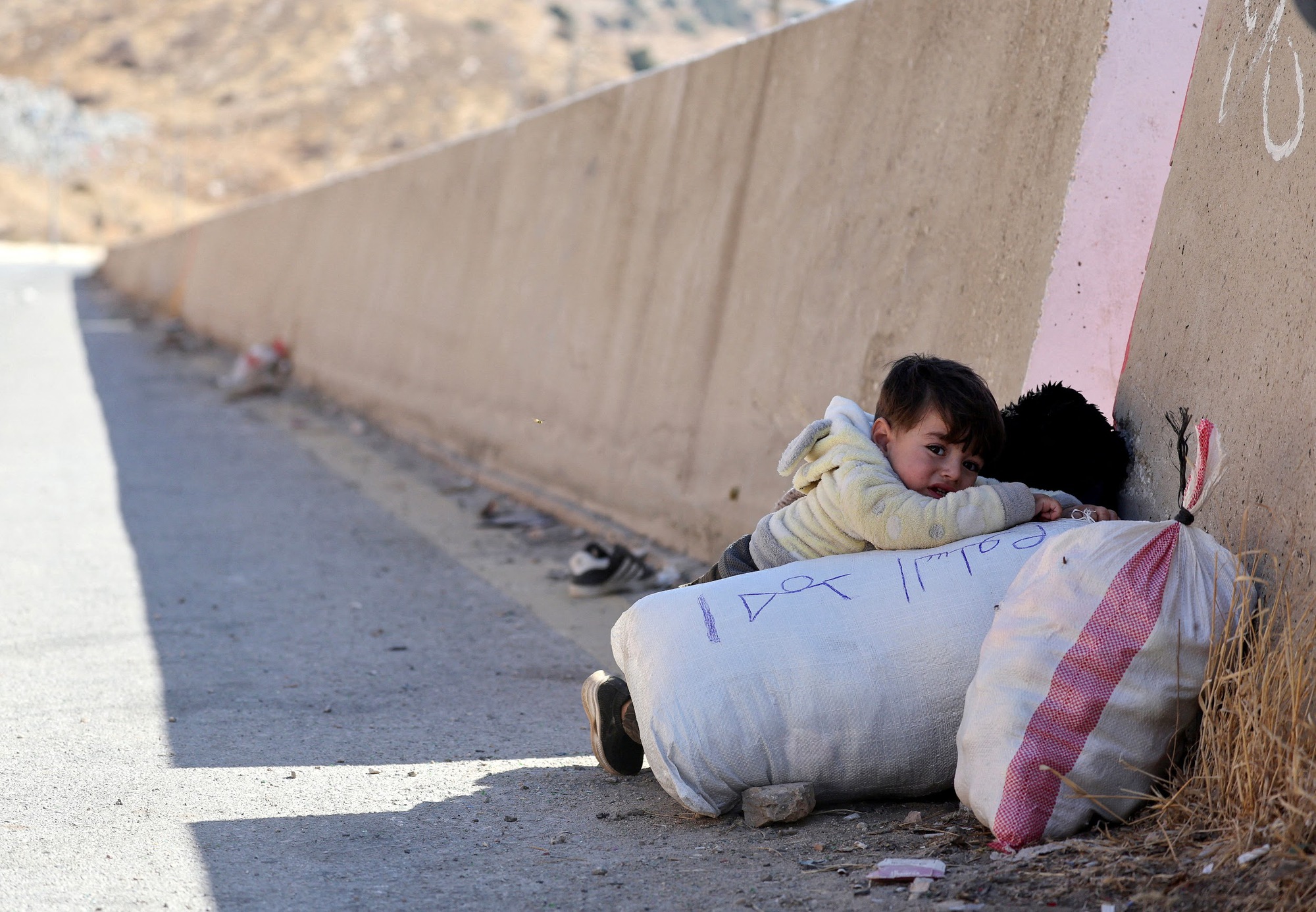 A child holds onto their belongings while crossing from Lebanon into Syria, as people flee the ongoing hostilities between Hezbollah and Israeli forces, at Masnaa border crossing