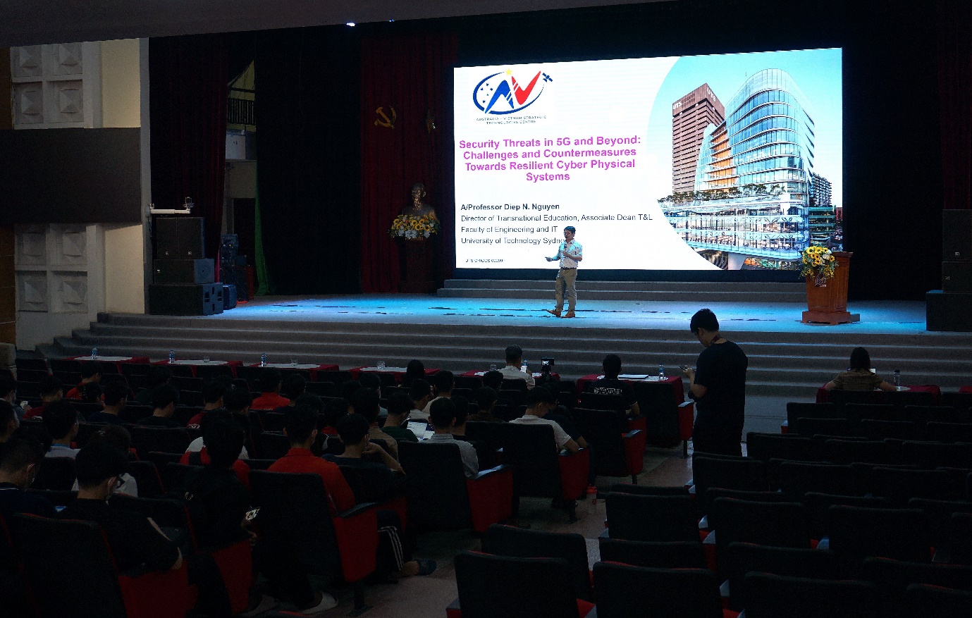 Những thách thức mới về an ninh mạng 5G cho hạ tầng số- Ảnh 3. A person standing on stage with a large screen Description automatically generated