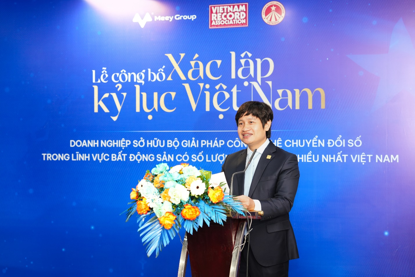 Kỷ lục Việt Nam xướng tên Meey Group với bộ giải pháp công nghệ lĩnh vực bất động sản có số lượng sản phẩm nhiều nhất- Ảnh 1. A person standing at a podium with a bouquet of flowers Description automatically generated