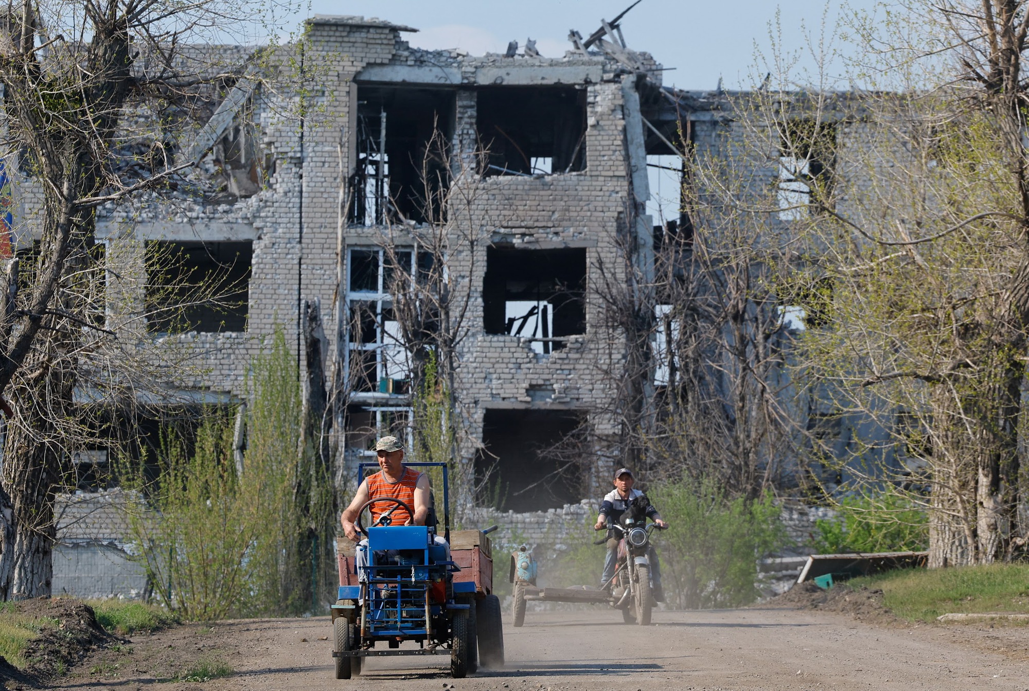 Men ride vehicles near a destroyed building in Toshkivka amid Russia-Ukraine conflict