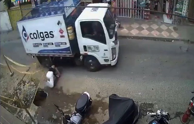 Người phụ nữ bế con bất ngờ vấp ngã, suýt bị bánh xe tải cán trúng - Ảnh 1.